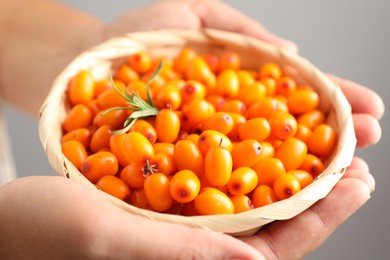 Photo of Woman with ripe sea buckthorn berries against grey background, closeup