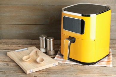 Photo of Yellow air fryer and kitchen utensils on wooden table