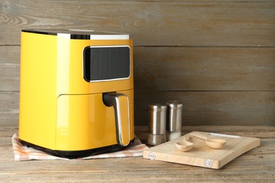 Photo of Yellow air fryer and kitchen utensils on wooden table. Space for text