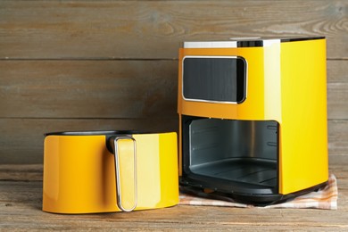 Photo of Yellow air fryer on wooden table. Modern kitchen appliance