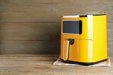Photo of Yellow air fryer on wooden table, space for text. Modern kitchen appliance