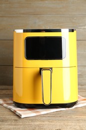 Photo of Yellow air fryer on wooden table. Modern kitchen appliance