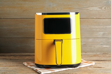 Photo of Yellow air fryer on wooden table. Modern kitchen appliance