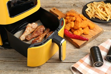 Photo of Modern air fryer and cooked meals on wooden table, closeup