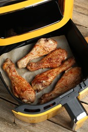 Photo of Air fryer with cooked chicken drumsticks on wooden table, above view