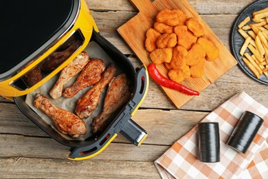 Photo of Modern air fryer and cooked meals on wooden table, flat lay