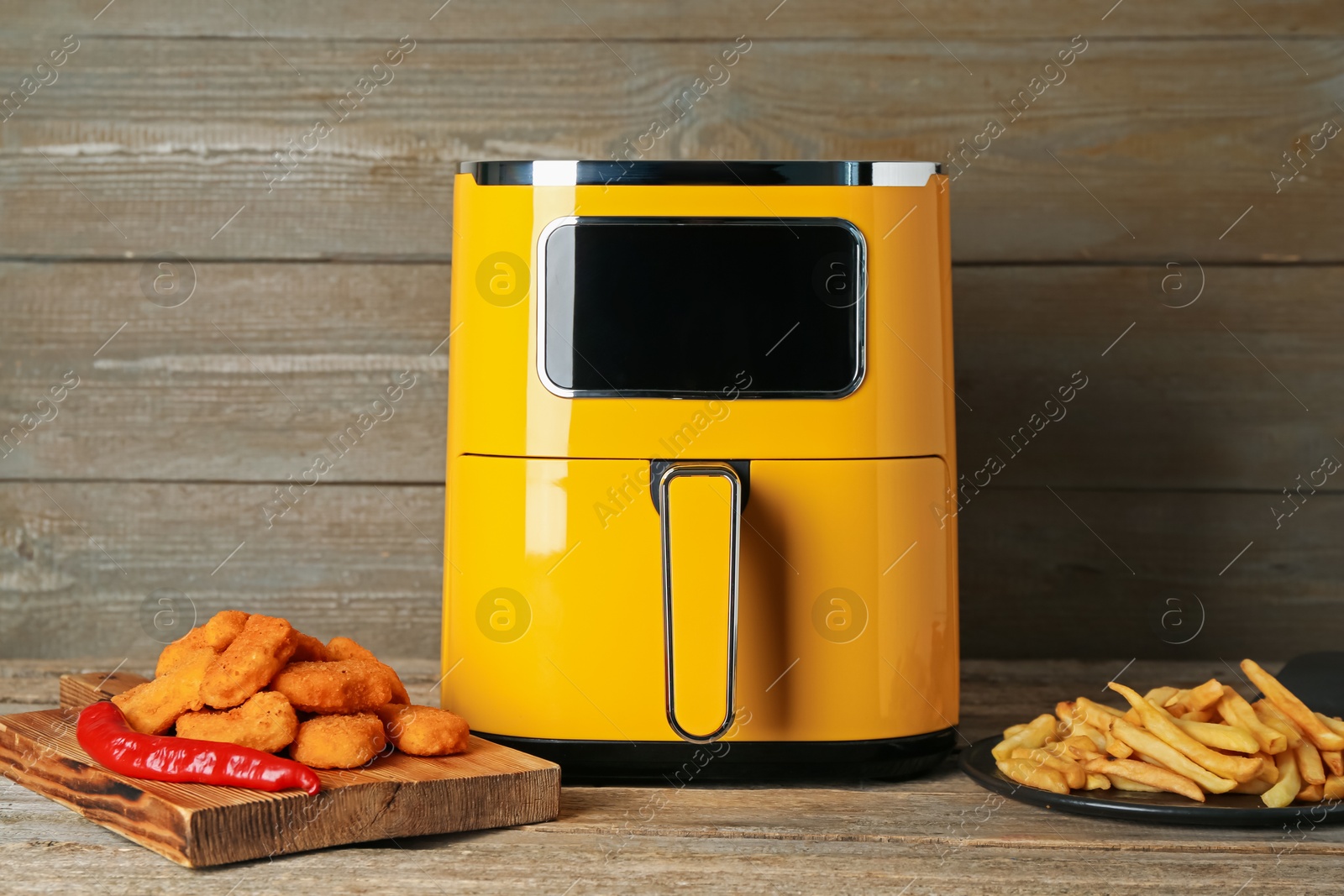 Photo of Modern air fryer, cooked chicken nuggets and french fries on wooden table