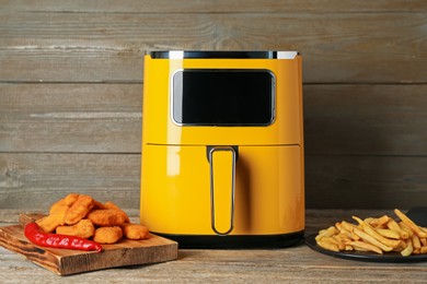 Photo of Modern air fryer, cooked chicken nuggets and french fries on wooden table