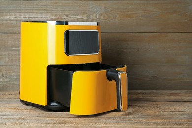 Photo of Yellow air fryer on wooden table, space for text. Modern kitchen appliance