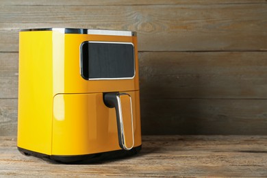 Photo of Yellow air fryer on wooden table, space for text. Modern kitchen appliance
