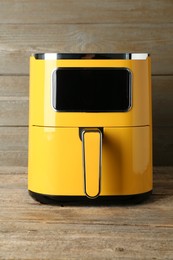 Photo of Yellow air fryer on wooden table. Modern kitchen appliance