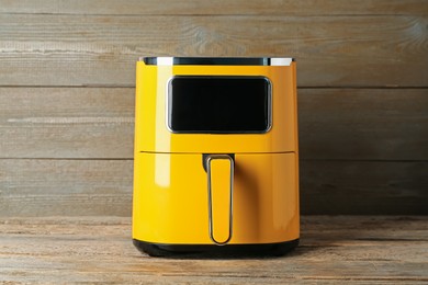 Photo of Yellow air fryer on wooden table. Modern kitchen appliance