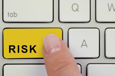 Image of Woman pressing yellow button with word Risk on computer keyboard, top view