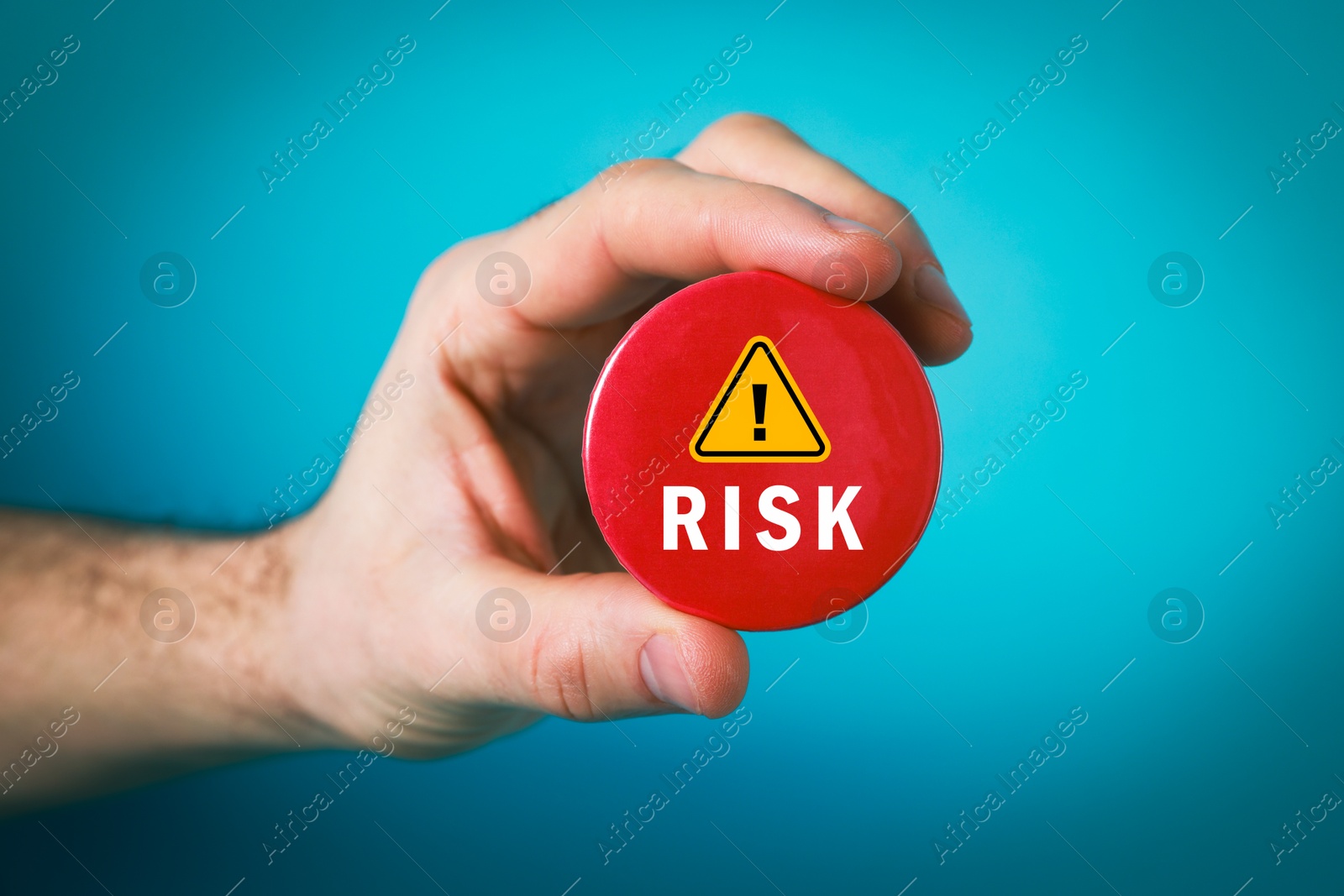 Man holding red button badge with word Risk and warning sign on light blue background, closeup Image of Man holding red button badge with word Risk and warning sign on light blue background, closeup