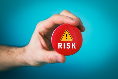 Image of Man holding red button badge with word Risk and warning sign on light blue background, closeup