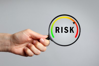 Image of Woman holding magnifying glass with word Risk and scale inside on grey background, closeup