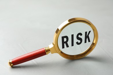 Image of Magnifying glass with word Risk inside against grey background