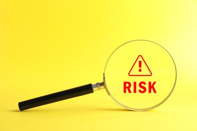 Image of Magnifying glass with word Risk and warning sign inside against yellow background