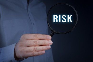 Image of Woman holding magnifying glass with word Risk inside against dark background, closeup