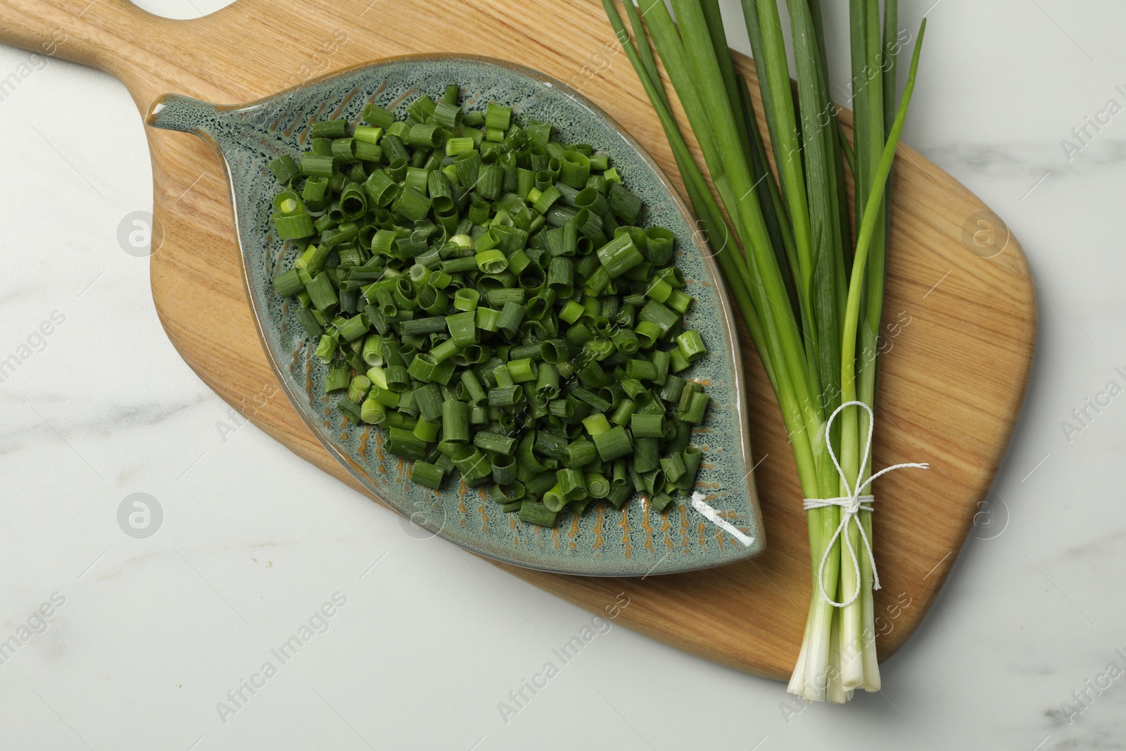 Photo of Chopped green spring onion and stems on white marble table, top view
