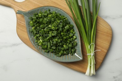 Photo of Chopped green spring onion and stems on white marble table, top view