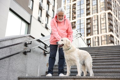 Photo of Elderly man with his adorable Golden Retriever dog on stairs outdoors, low angle view