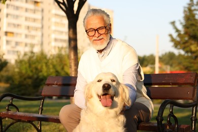Photo of Portrait of elderly man in glasses with adorable Golden Retriever dog on bench outdoors