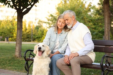 Photo of Happy senior couple with adorable Golden Retriever dog on bench outdoors