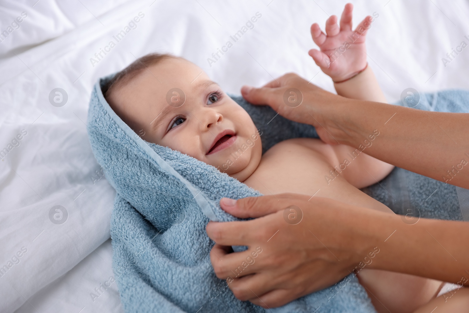 Photo of Mother wrapping her cute little baby with towel after bathing on bed, closeup
