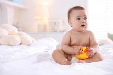 Photo of Cute baby with rubber duck after bathing on bed at home, space for text