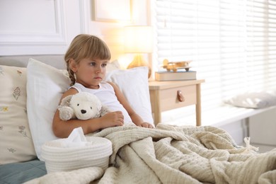 Photo of Sick little girl with her toy and tissues in bed at home. Space for text