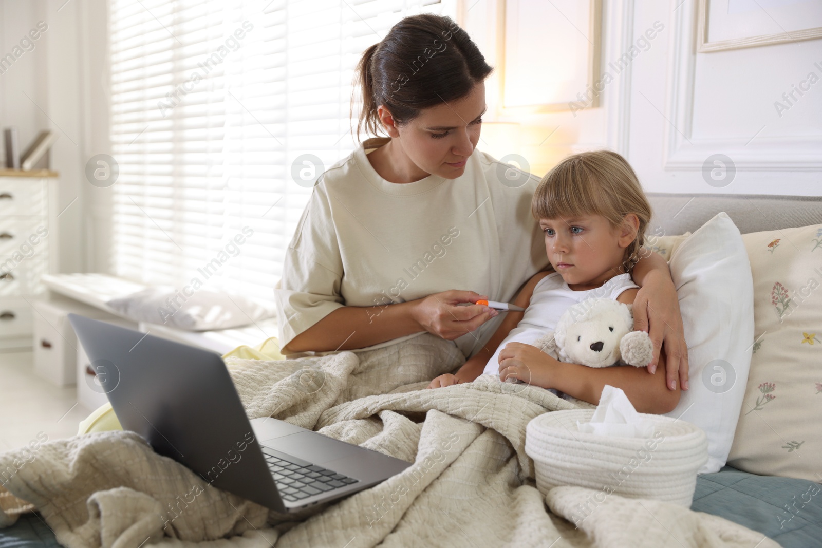 Photo of Telehealth. Mother and her sick daughter having online consultation with doctor via laptop on bed at home