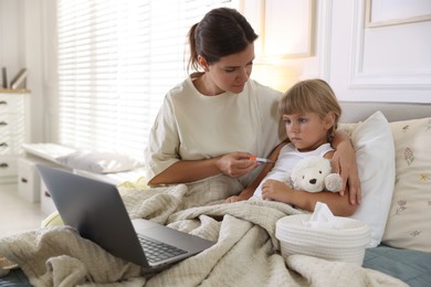 Photo of Telehealth. Mother and her sick daughter having online consultation with doctor via laptop on bed at home
