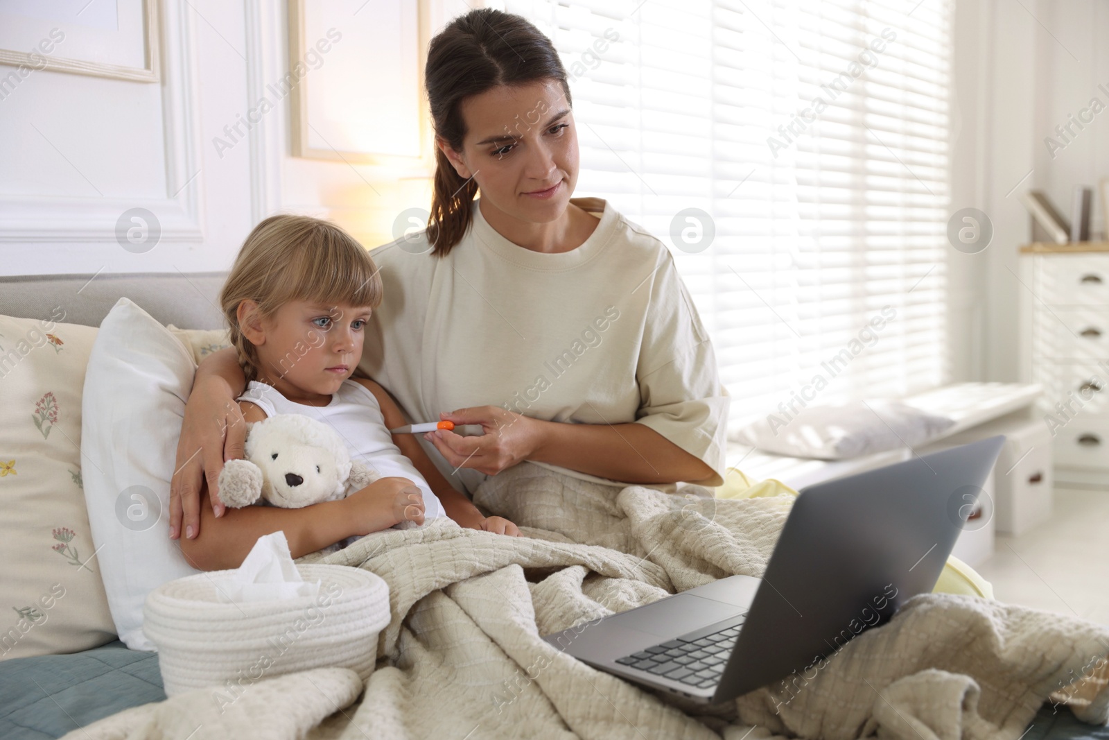 Photo of Telehealth. Mother and her sick daughter having online consultation with doctor via laptop on bed at home