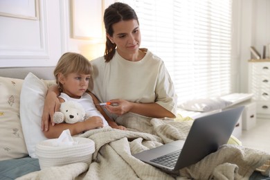 Photo of Telehealth. Mother and her sick daughter having online consultation with doctor via laptop on bed at home
