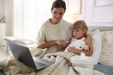 Photo of Telehealth. Mother and her sick daughter having online consultation with doctor via laptop on bed at home