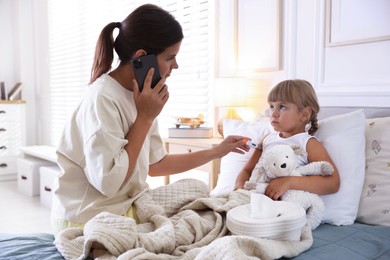 Photo of Telehealth. Mother and her sick daughter having consultation with doctor via phone on bed at home