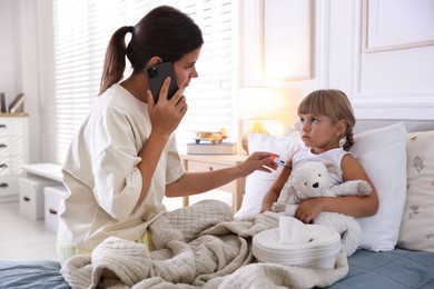 Photo of Telehealth. Mother and her sick daughter having consultation with doctor via phone on bed at home