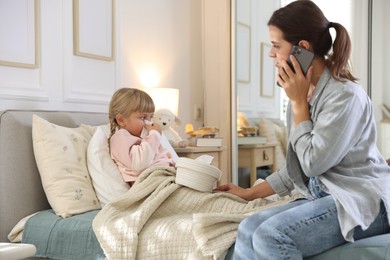 Photo of Telehealth. Mother and her sick daughter having consultation with doctor via phone on bed at home