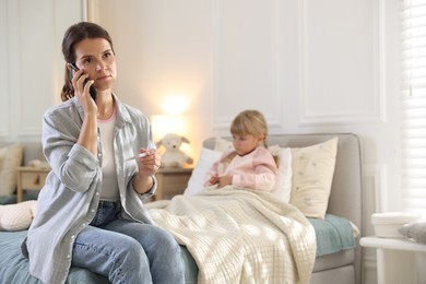 Photo of Telehealth. Mother and her sick daughter having consultation with doctor via phone on bed at home, selective focus