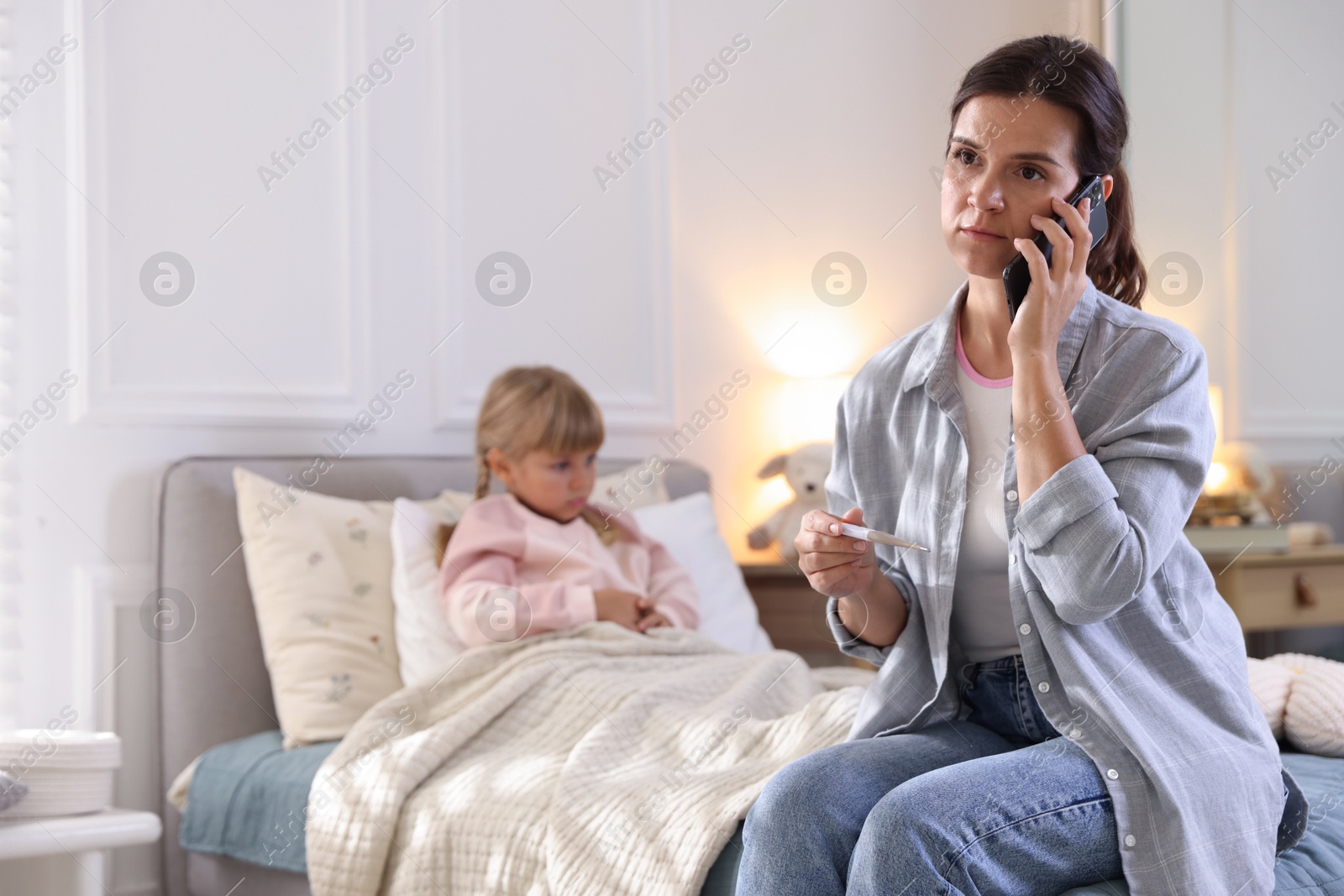 Photo of Telehealth. Mother and her sick daughter having consultation with doctor via phone on bed at home, selective focus