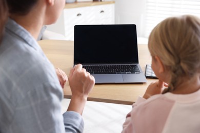 Photo of Telehealth. Mother and her daughter having online consultation with doctor via laptop at table indoors, back view