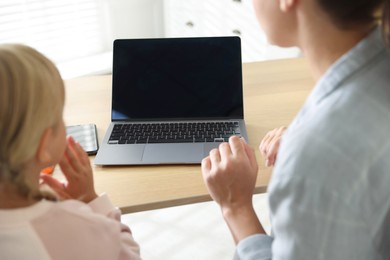 Photo of Telehealth. Mother and her daughter having online consultation with doctor via laptop at table indoors, back view