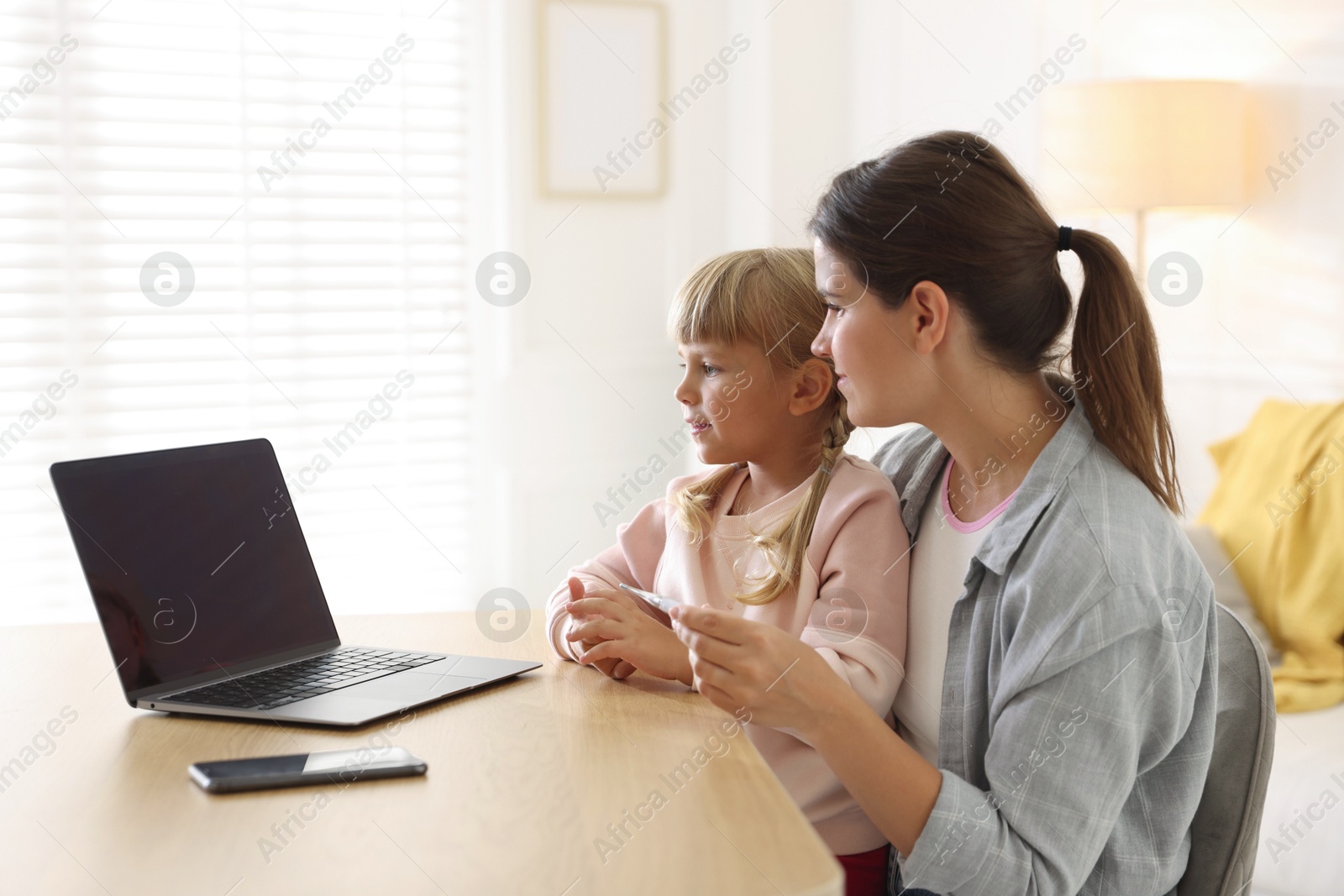 Photo of Telehealth. Mother and her daughter having online consultation with doctor via laptop at table indoors