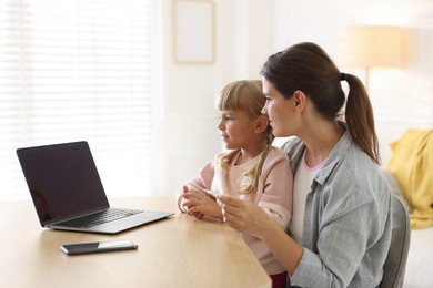 Photo of Telehealth. Mother and her daughter having online consultation with doctor via laptop at table indoors