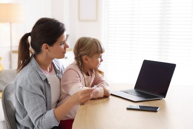 Photo of Telehealth. Mother and her daughter having online consultation with doctor via laptop at table indoors