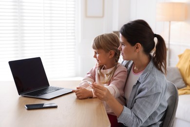 Photo of Telehealth. Mother and her daughter having online consultation with doctor via laptop at table indoors