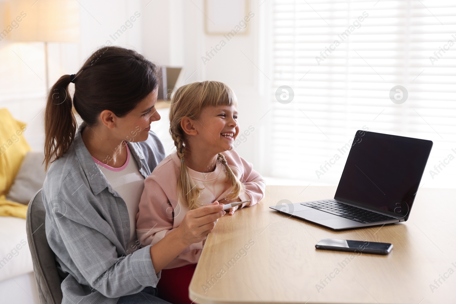 Photo of Telehealth. Mother and her daughter having online consultation with doctor via laptop at table indoors