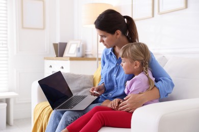 Photo of Telehealth. Mother and her sick daughter having online consultation with doctor via laptop on sofa at home