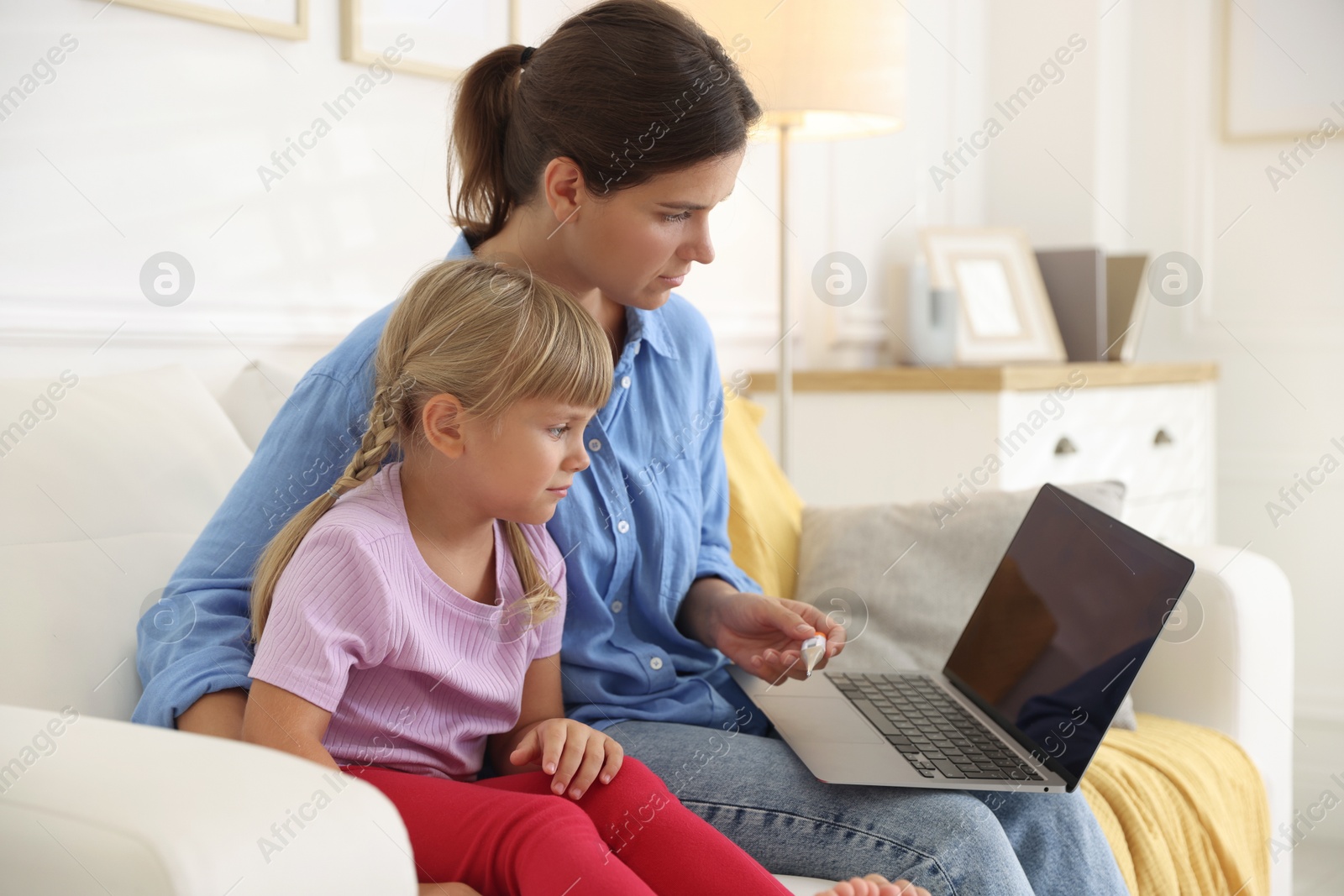Photo of Telehealth. Mother and her sick daughter having online consultation with doctor via laptop on sofa at home